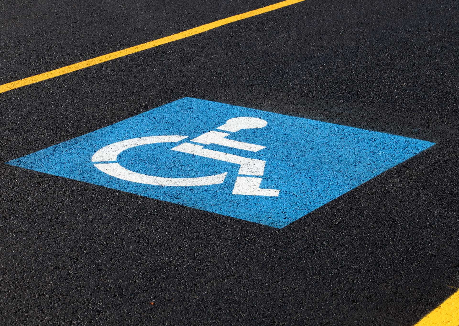 Blue wheelchair symbol on black asphalt, yellow parking lines.