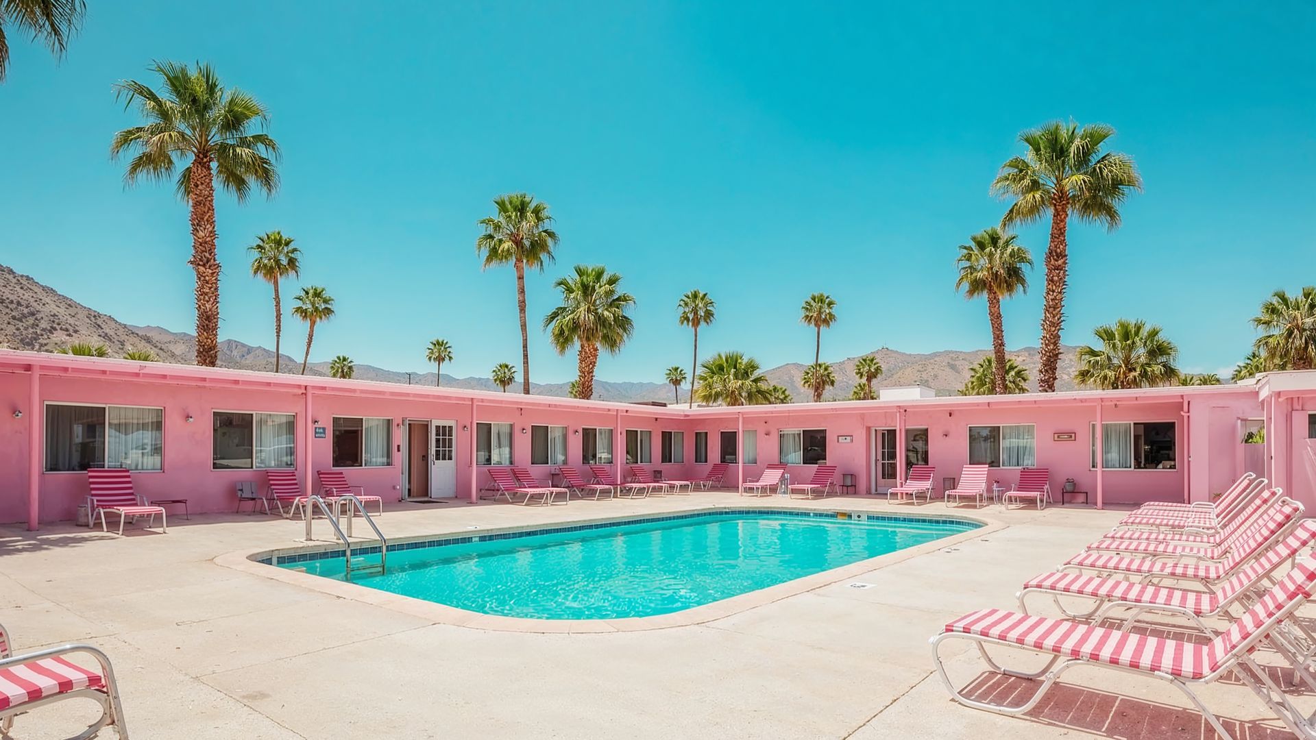 Pink motel with pool and palm trees under a clear blue sky.