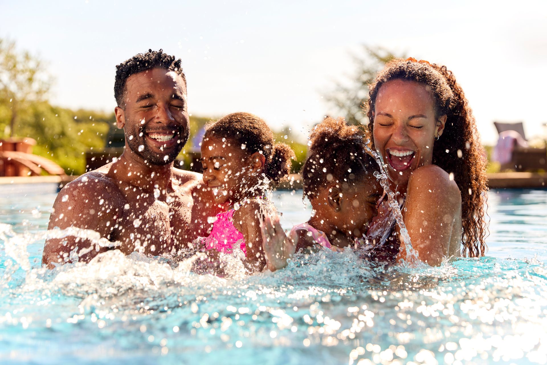 Family of four splashing in a pool, laughing and enjoying themselves in the sun.