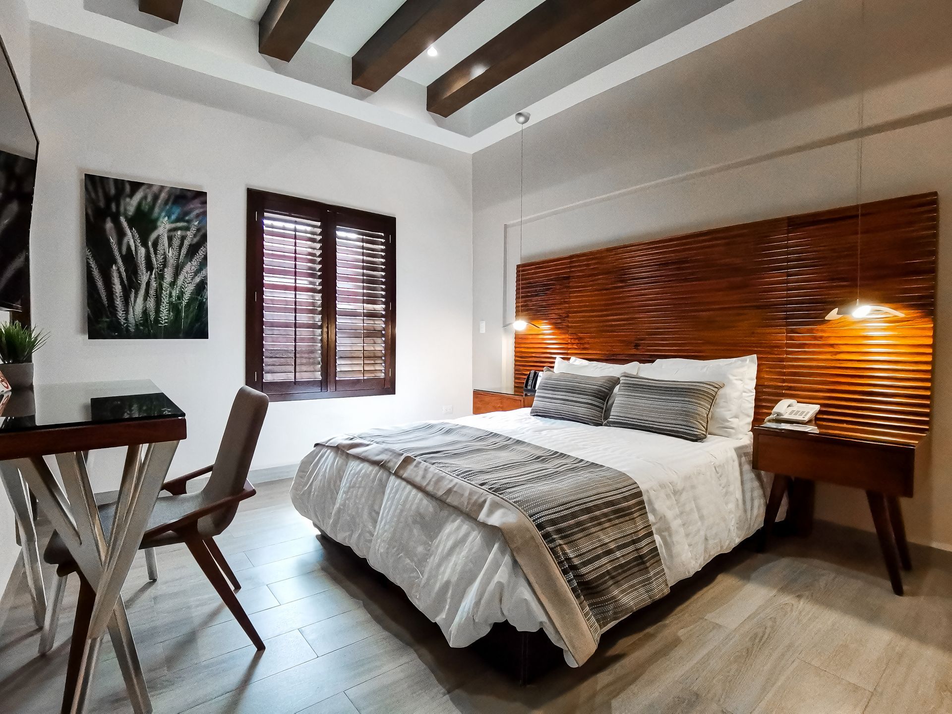 Un dormitorio con una cama, escritorio, silla y persianas en las ventanas.