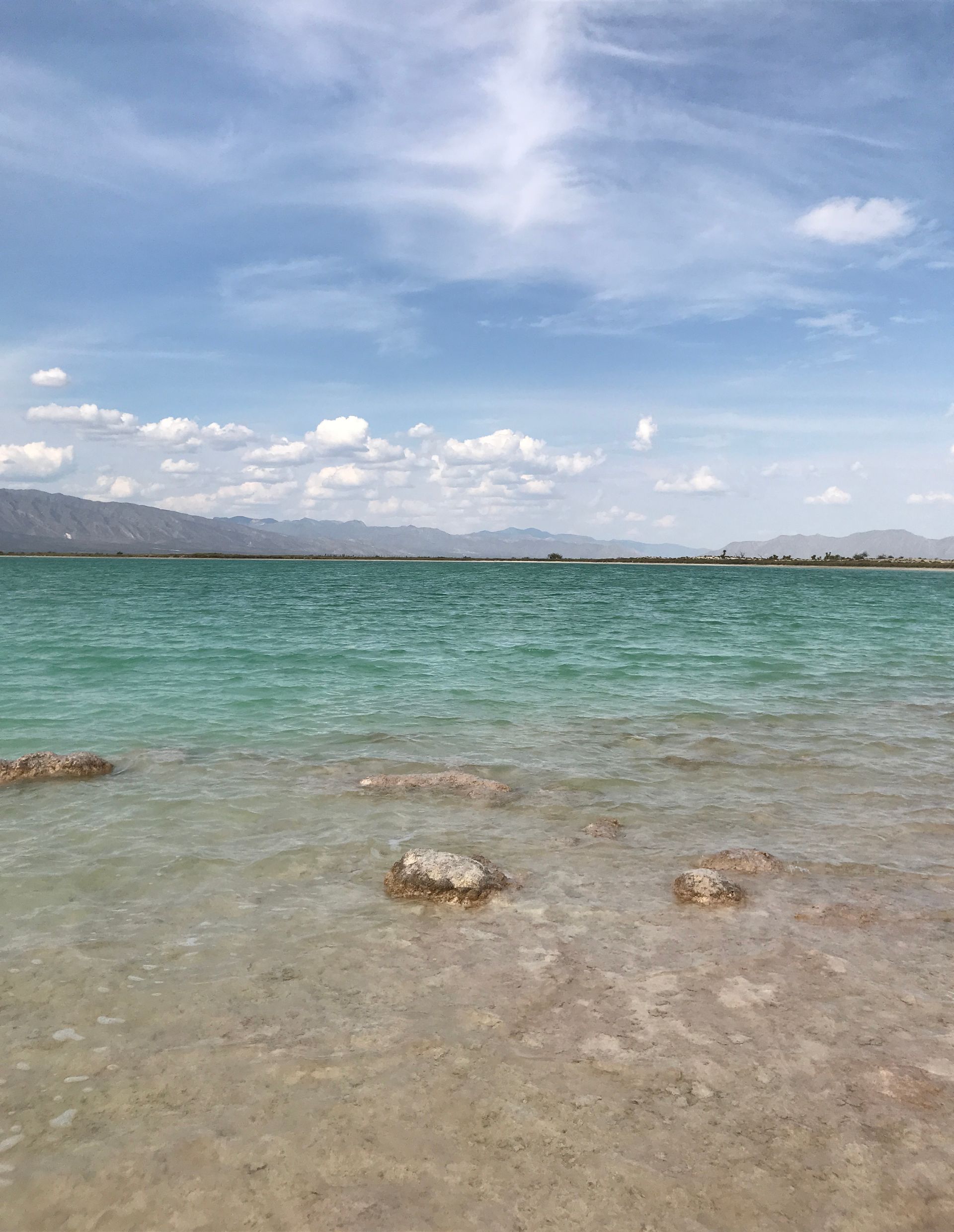 Una gran masa de agua con montañas al fondo en un día soleado.