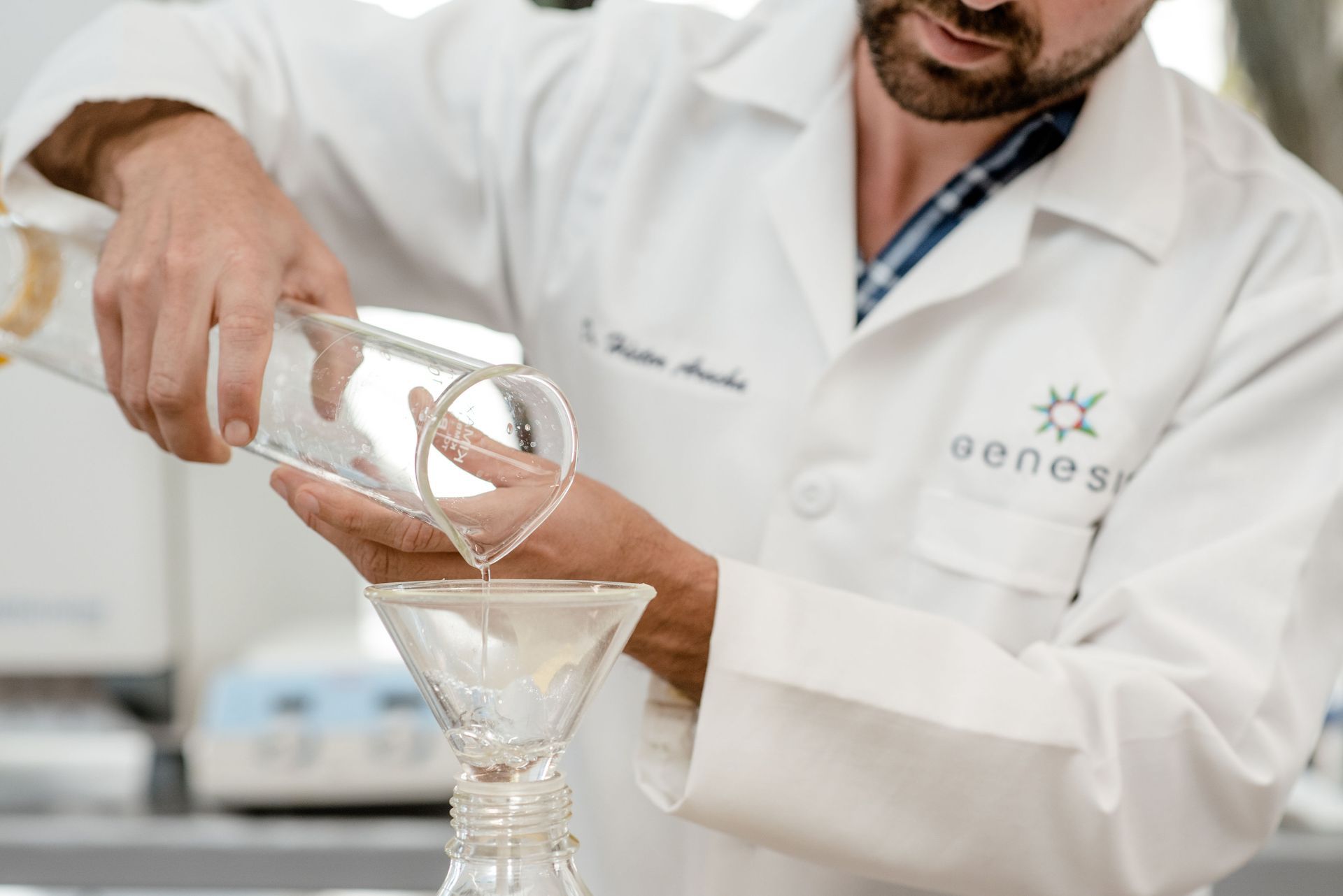 Hombre con bata de laboratorio vierte líquido de un vaso de precipitados a través de un embudo en un matraz de vidrio.