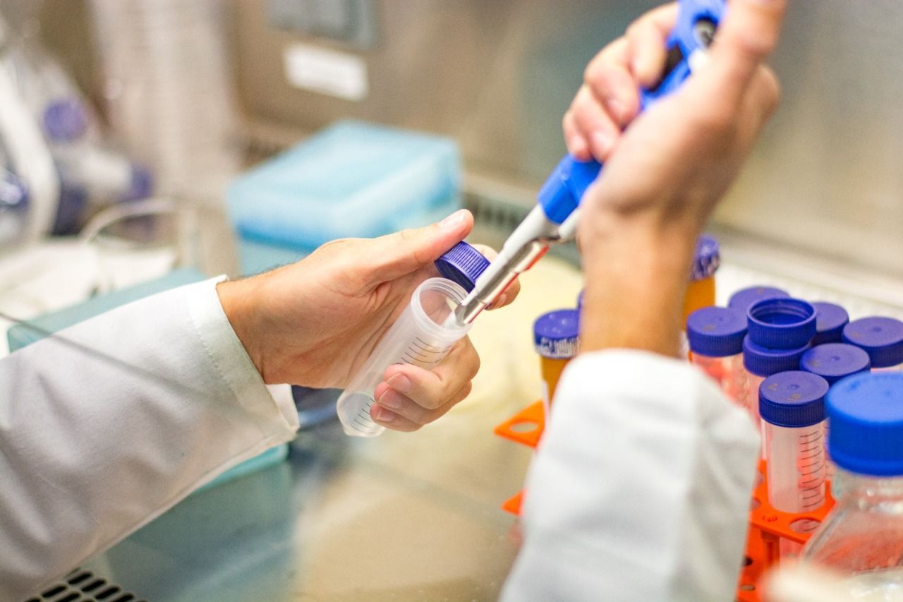 Científico que utiliza una pipeta para transferir líquido a un tubo de ensayo dentro de un entorno de laboratorio.