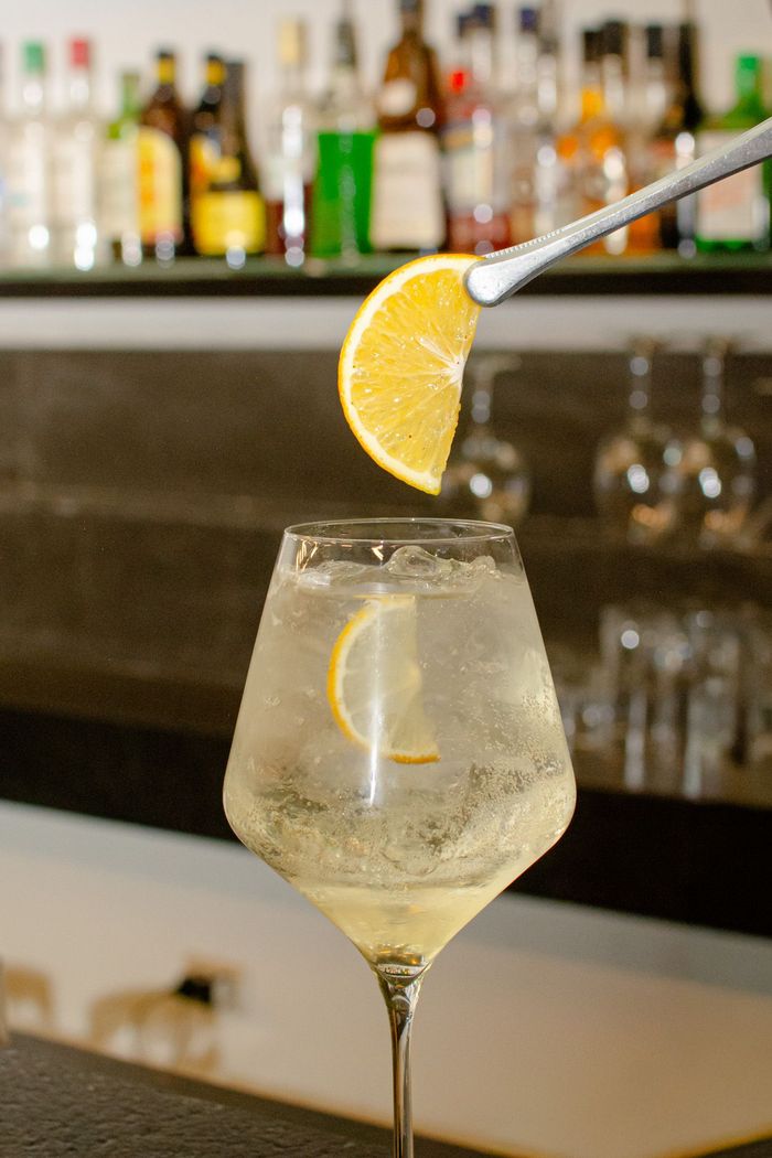 Un camarero decora un cóctel con una rodaja de naranja. La bebida se sirve en un vaso transparente sobre la barra.