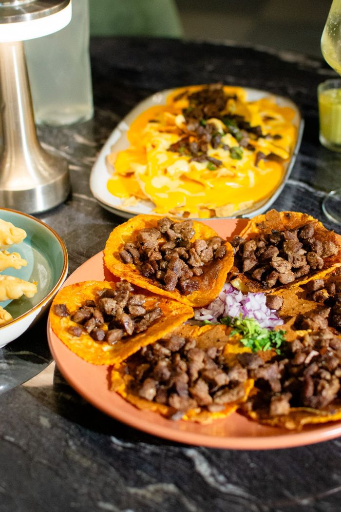 Plato de tacos con carne y un acompañamiento de nachos con queso.