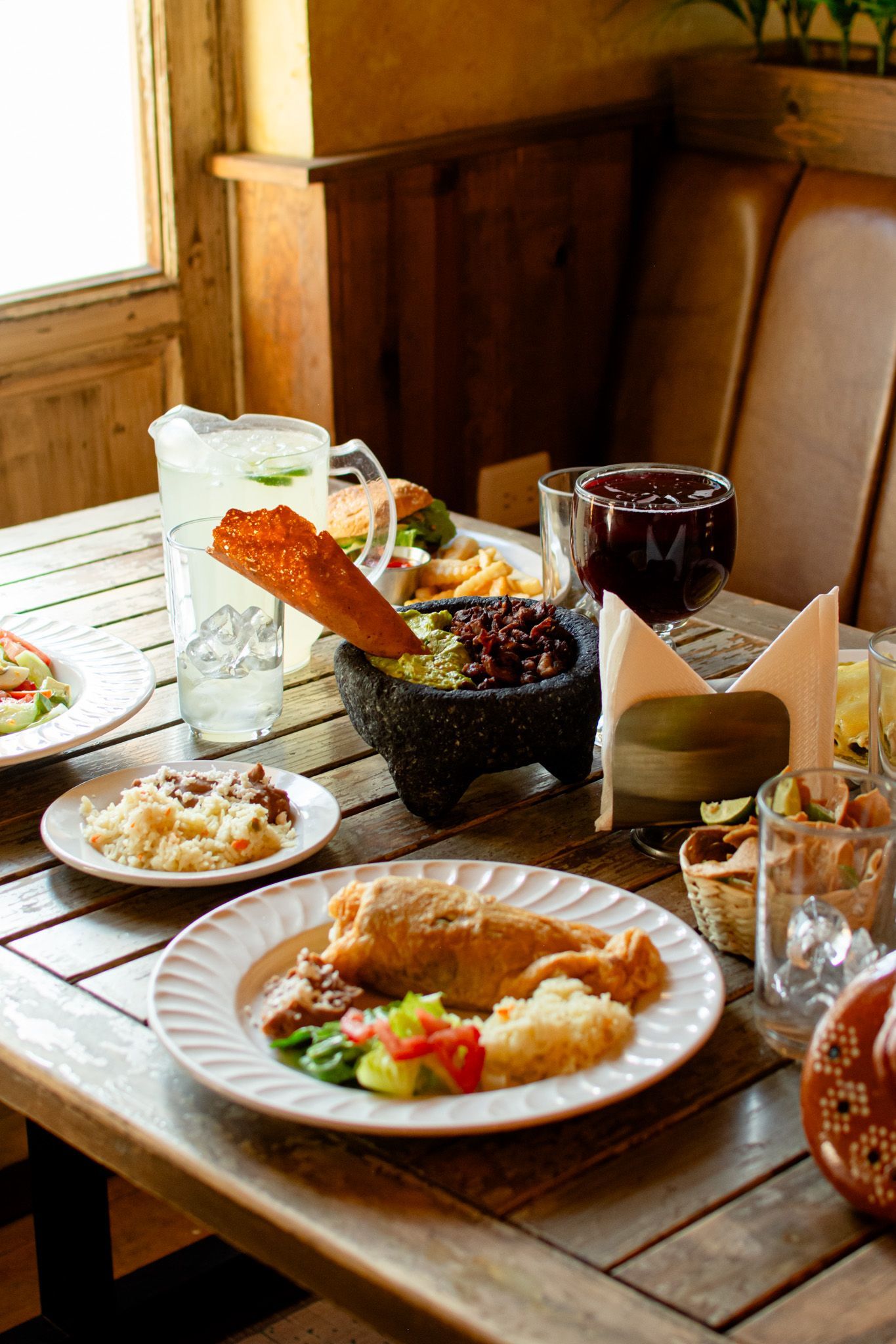 Mesa puesta con comida mexicana: enchilada, arroz, frijoles, guacamole, bebidas y tortillas.