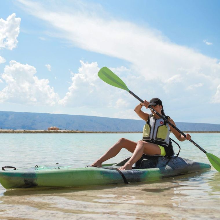 Mujer haciendo kayak en aguas cristalinas con chaleco salvavidas. Día soleado y cielo azul.