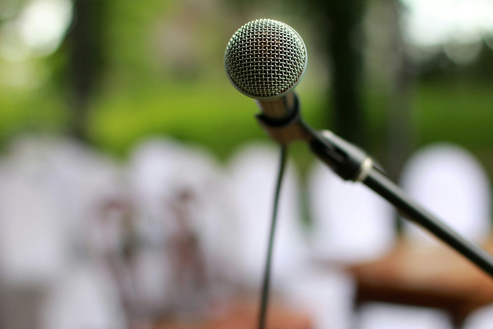 A microphone on a stand against a blurred outdoor background with white chairs.
