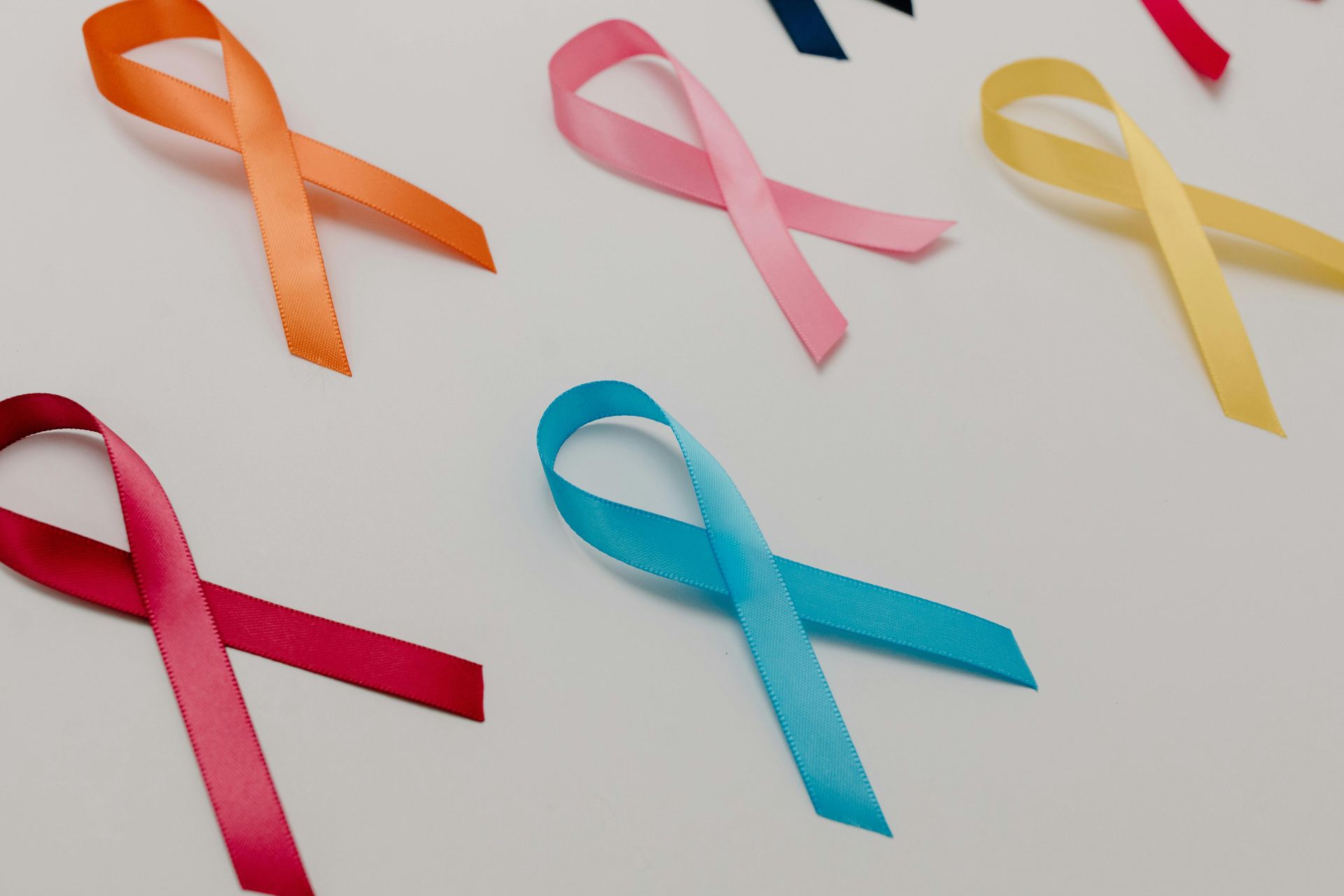 Several awareness ribbons in various colors, including orange, pink, yellow, red, and blue, arranged on a white background.