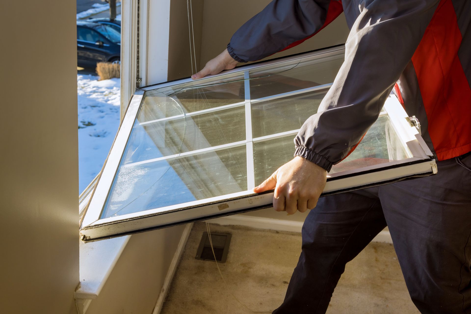 Person carrying a large window frame through a doorway into a snowy yard