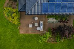 Overhead view of a wooden patio beside a house with outdoor furniture, surrounded by green lawn and shrubs