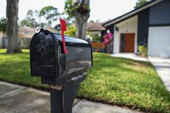 Black mailbox with a red flag by a suburban driveway and house.