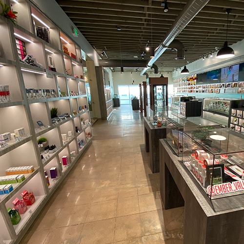 Interior of a brightly lit cannabis dispensary with product displays on shelves and tables.