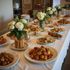 Table de buffet avec divers plats et compositions florales sur une nappe blanche.