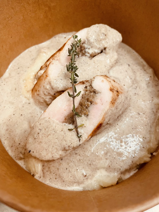 Roulade de poulet avec farce, sauce crémeuse et brin d'herbes, dans un bol.