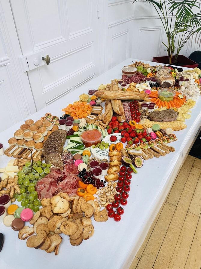 Longue table dressée avec charcuterie, pain, fruits et collations.