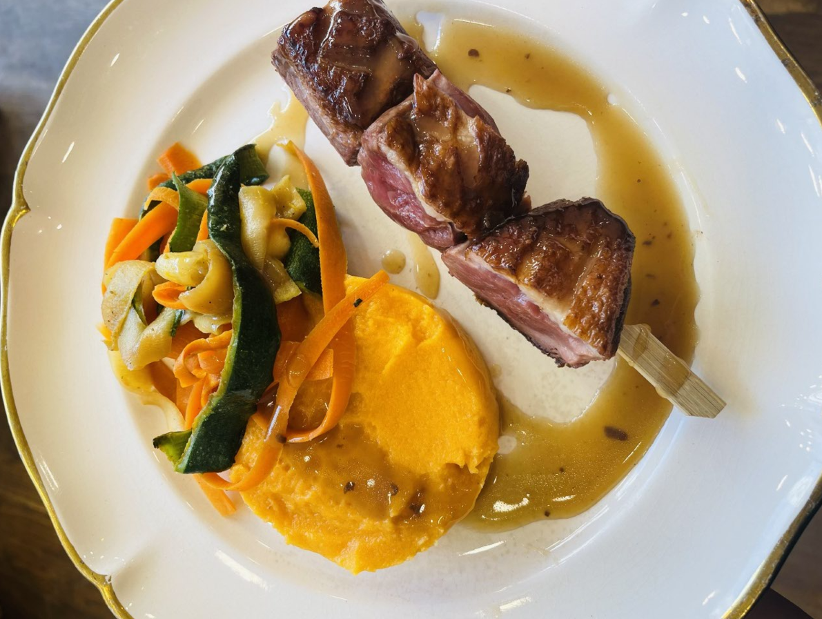 Brochettes de canard avec patate douce et légumes sur une assiette blanche avec sauce.