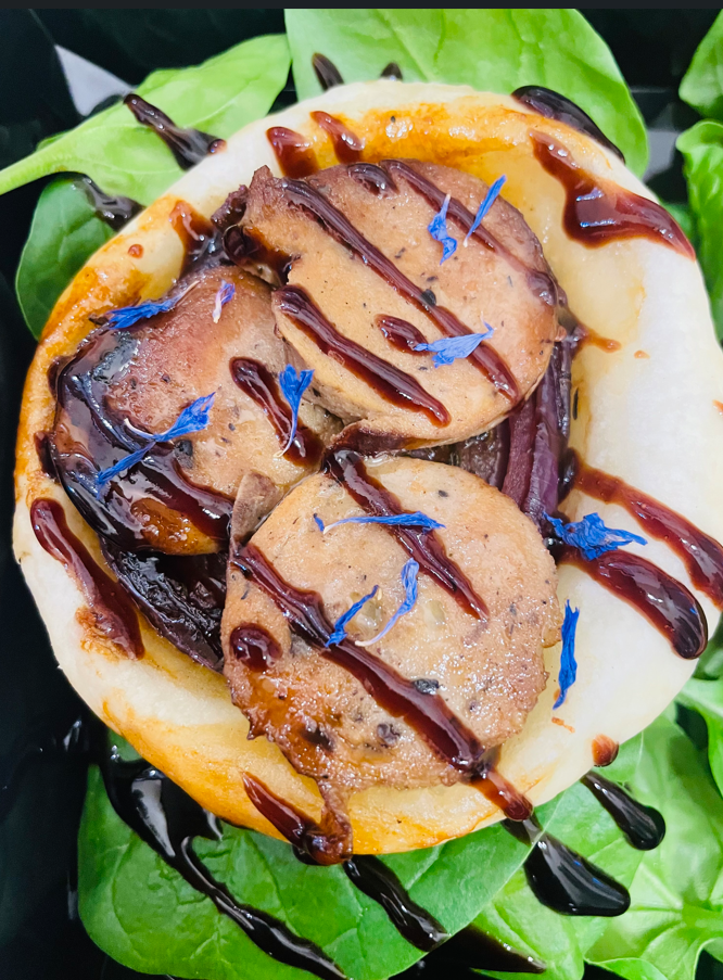 Bao bun avec médaillons poêlés, arrosé de sauce, sur épinards et garni de pétales bleus.