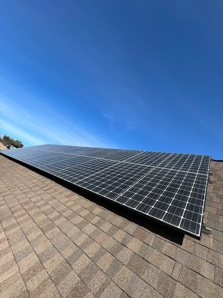 Solar panels mounted on a shingled roof under a clear blue sky