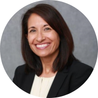 Professional headshot of a smiling woman in a black blazer against a gray background