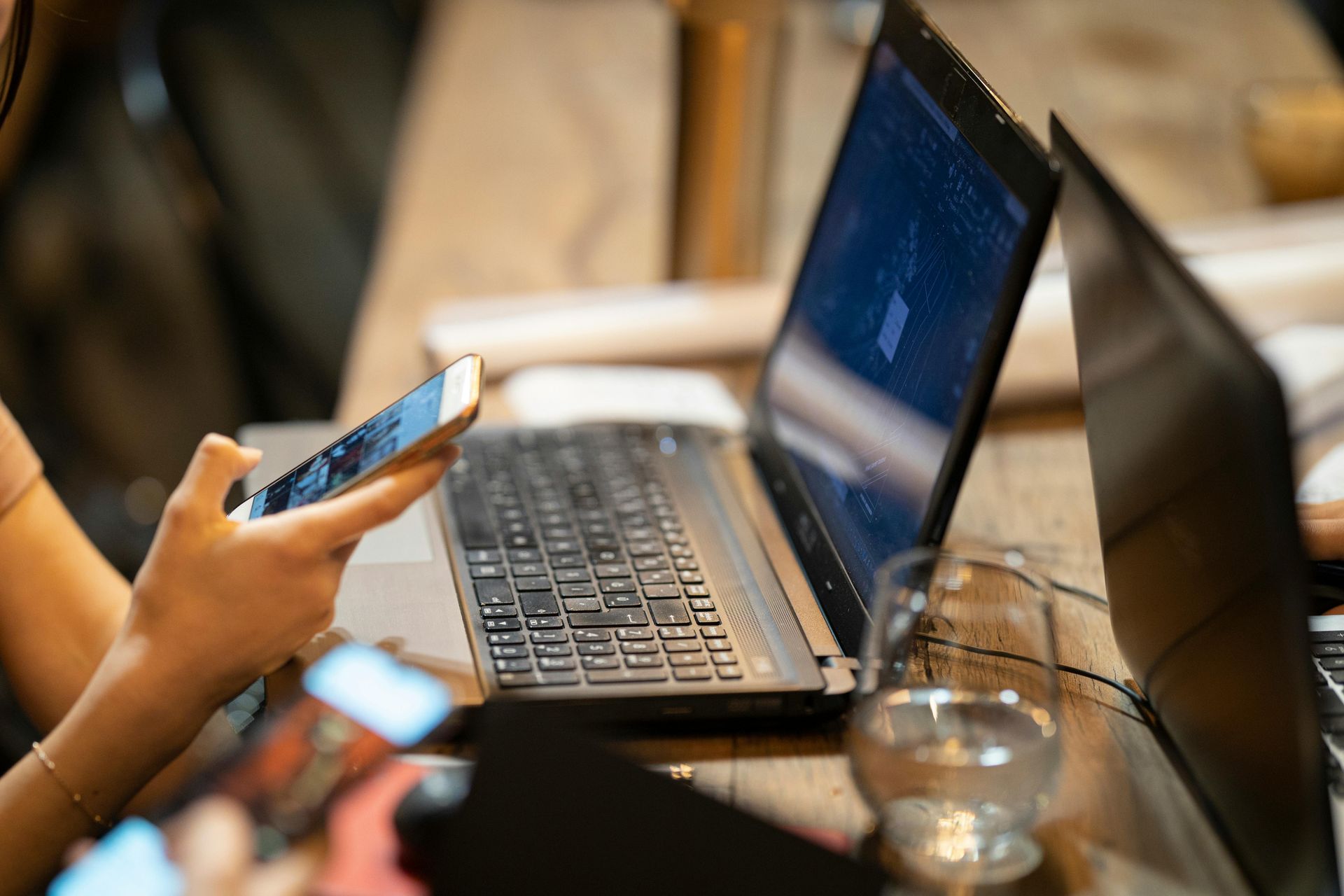 Hands using smartphones beside a laptop on a table in a café-like setting
