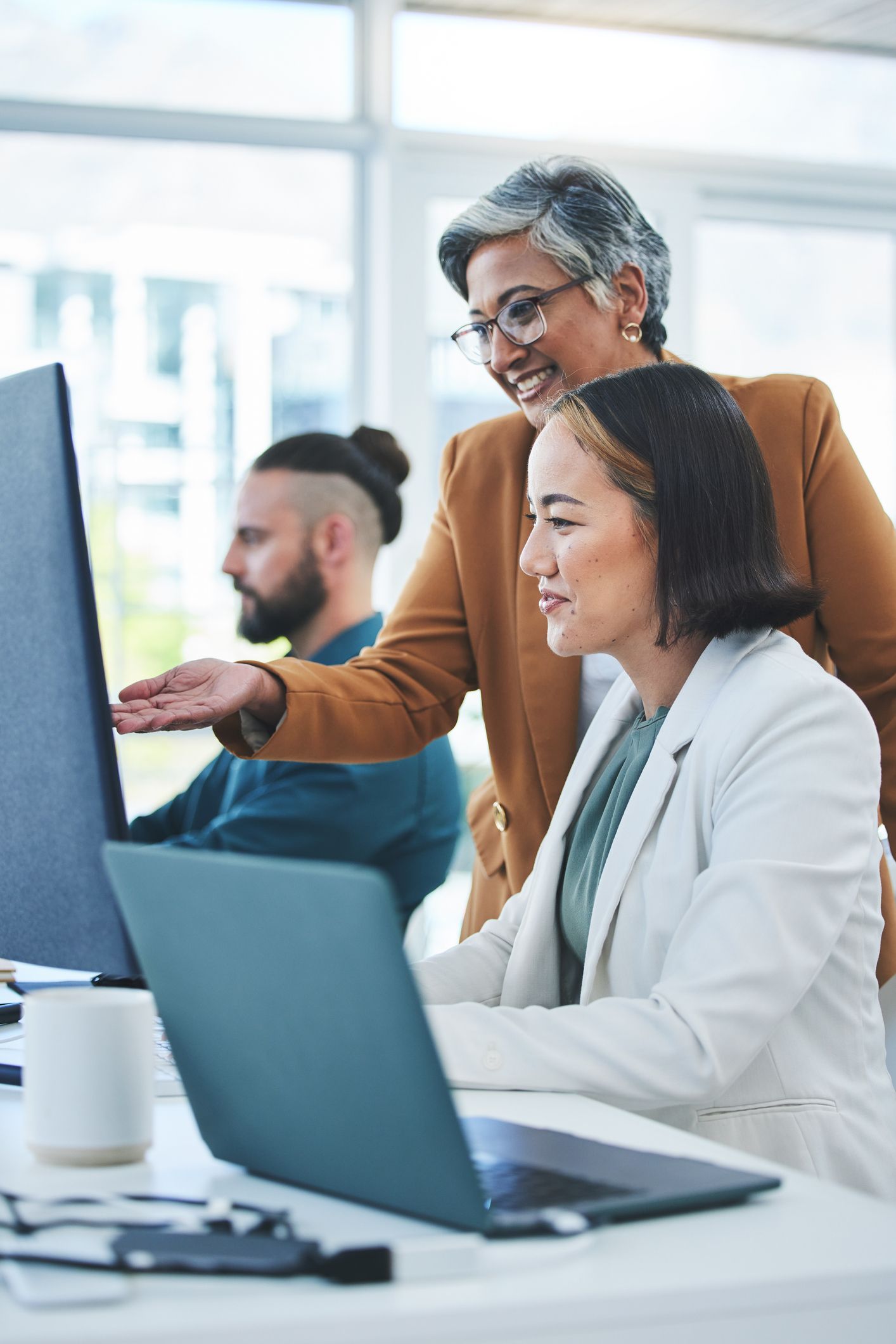 Three coworkers collaborating at a laptop in a bright office
