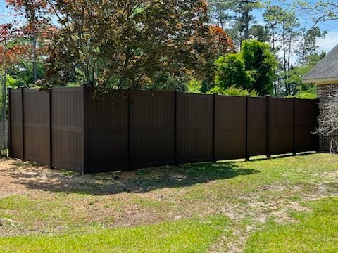 Brown privacy fence in a backyard, surrounded by green grass and trees.
