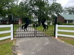 Black wrought iron gates with rearing horse silhouettes; white fence, driveway.