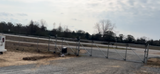 A gravel parking area with a gate and a treeline in the background on an overcast day.