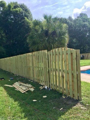 Wooden fence in yard with a pool, surrounded by trees and grass.