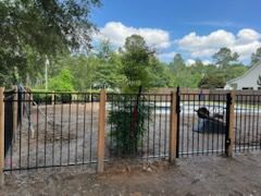 Black metal fence with wooden posts, in front of a yard with trees and a house.