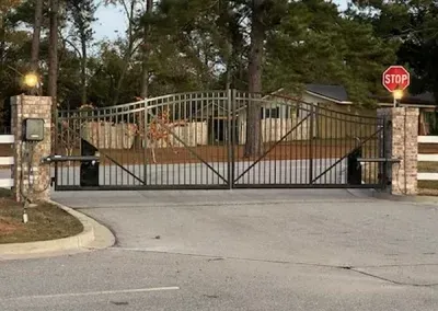Entrance gate with brick pillars and iron gates, featuring a stop sign on the right.