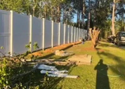 White privacy fence along a grassy area; a person's shadow is cast in the grass.