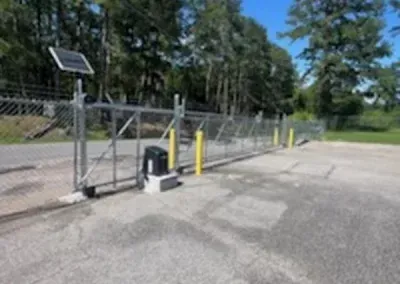 Solar-powered automatic gate, chain-link fence, gravel lot. A sunny day.