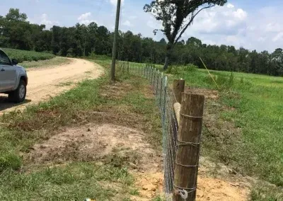 A dirt road with a wire fence and a pickup truck parked alongside a field.