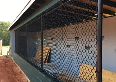 Black chain-link fence encloses a baseball dugout, with green and brown accents, under a roof.