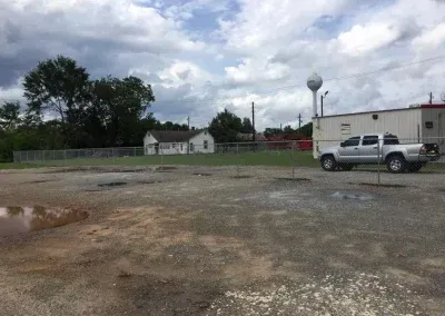 Gravel lot with a silver truck, a white building, and a water tower against a cloudy sky.