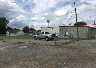 Silver pickup truck parked near a fence and building; water tower and cloudy sky in the background.