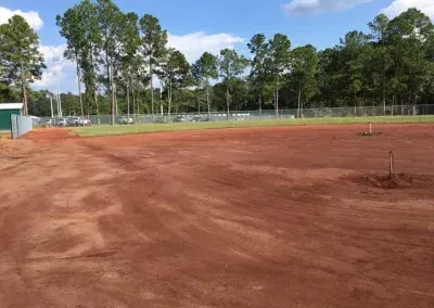 Red dirt baseball field under a blue sky, trees in background.