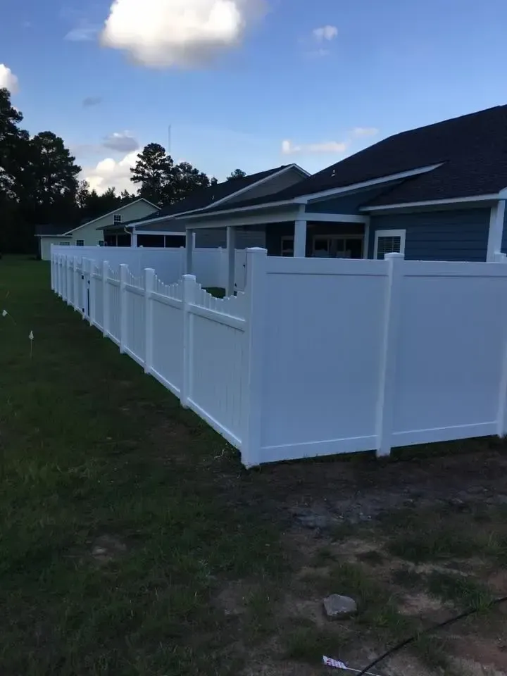 White vinyl fence in a grassy yard, alongside a blue house under a cloudy sky.