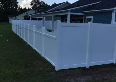 White vinyl fence enclosing a backyard with green grass and a blue house.