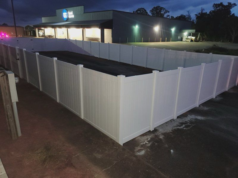 White vinyl fence encloses a rectangular area in front of a building at dusk.