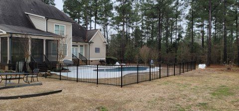 Backyard with a house, pool, and fence in a wooded area.