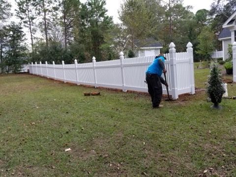 Black metal fence with wooden posts, in front of a yard with trees and a house.