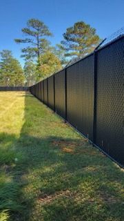 Black security fence with razor wire, green grass, blue sky.