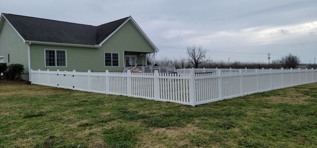 A white picket fence surrounds a green house on a cloudy day.
