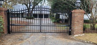 Black iron gate with brick pillars and driveway. A house is visible behind the gate.
