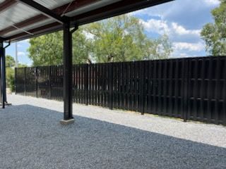 Black vertical fence along a gravel path, viewed from under a covered area.