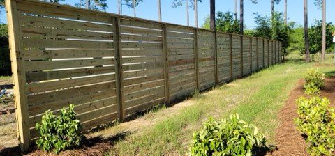 Wooden horizontal slat fence in a grassy yard with small shrubs.
