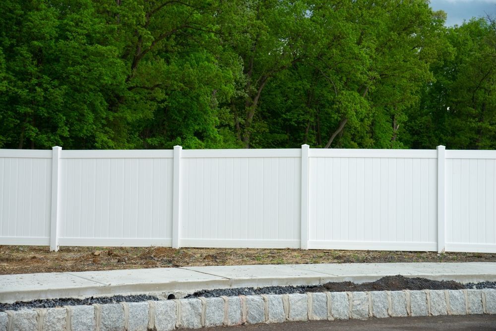 White vinyl fence against a backdrop of green trees.